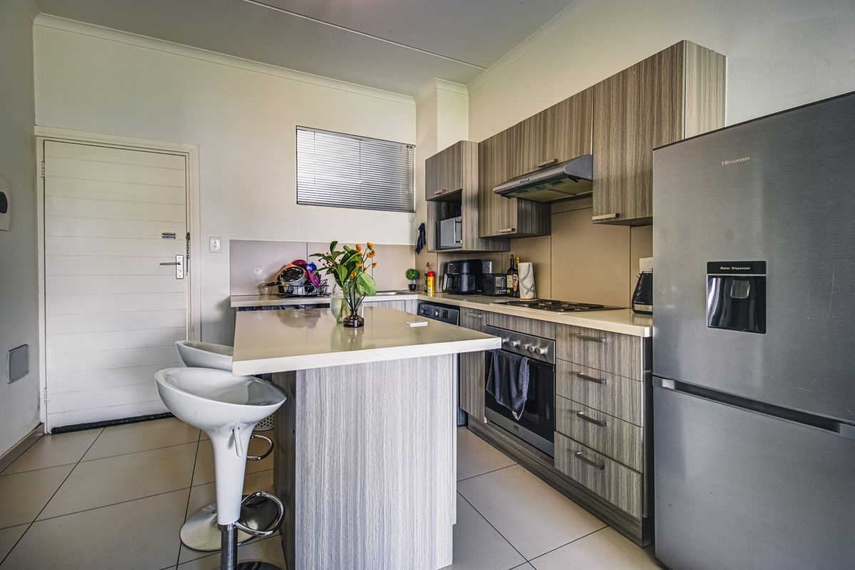 Modern kitchen featuring wood-grain cabinetry, stone countertops, a central island, and integrated appliances, finished with neutral tiled flooring.