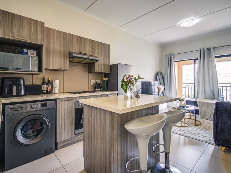 Modern open-plan kitchen and living area featuring wood-finish cabinetry, stone countertops, integrated appliances, and direct access to a private balcony.