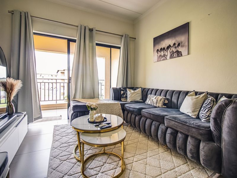 A well-lit living room featuring tiled floors and a sliding glass door providing direct access to an outdoor balcony.