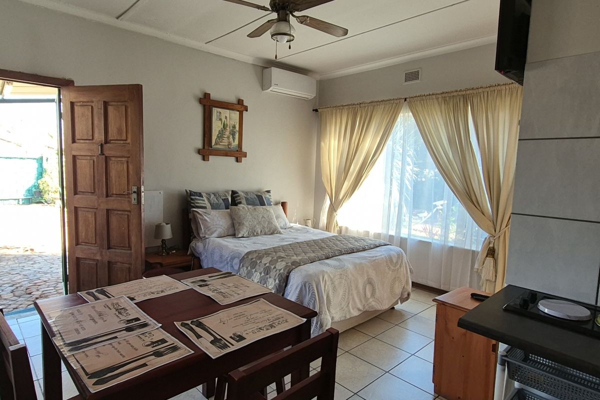 A functional bedroom featuring ceramic floor tiles, a ceiling fan, and a wall-mounted split-system air conditioner, with direct access to an outdoor area.