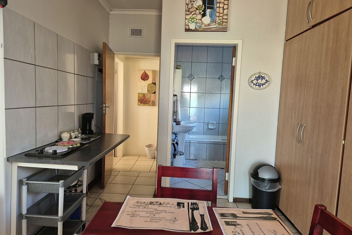 A functional kitchen area featuring built-in cabinetry, a tiled splashback, and a hob, with direct access to an adjacent bathroom.