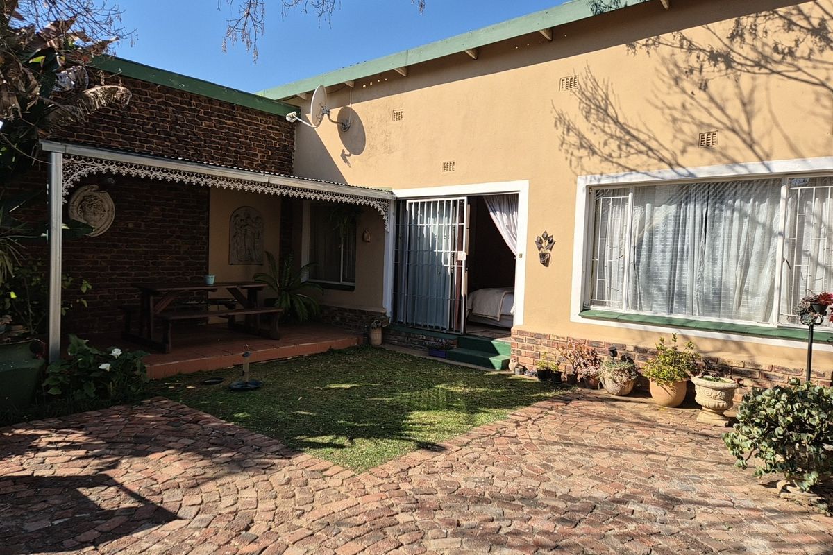 Rear exterior view featuring a covered patio area, brick paved courtyard, and direct access to the interior through a security gate.