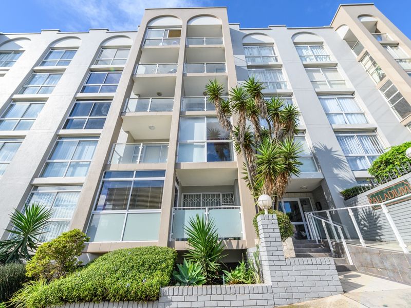 Low-angle view of the Palladium apartment building facade, featuring multiple levels of balconies with glass balustrades and a landscaped front garden area.