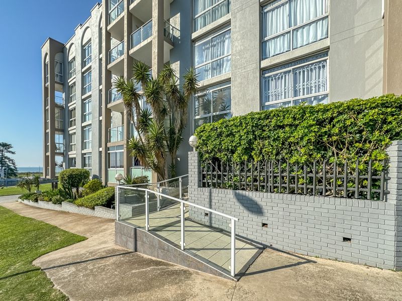 Exterior view of the apartment building facade featuring a paved accessibility ramp, glass balustrades, and established garden landscaping.
