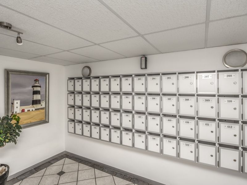 A clean and functional apartment building entrance lobby featuring a large wall-mounted bank of individual mailboxes and tiled flooring.