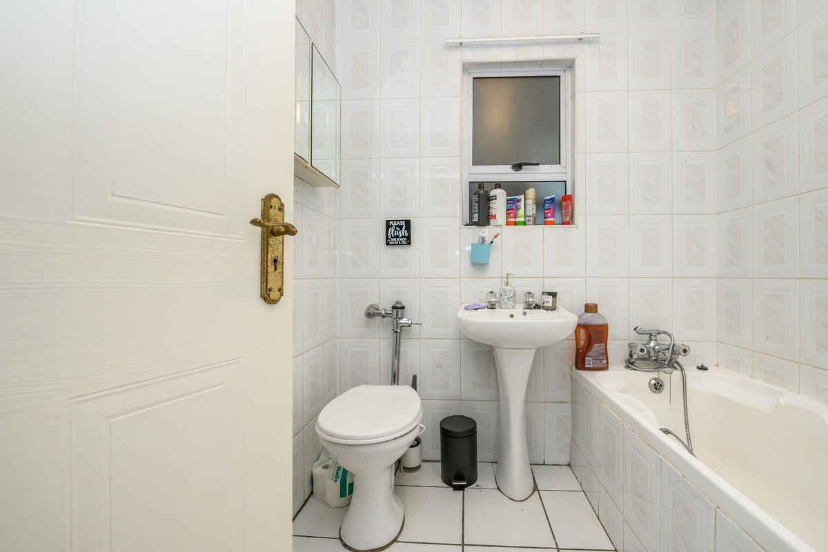 A compact bathroom featuring a pedestal basin, bathtub, and toilet with dated wall and floor tiling.
