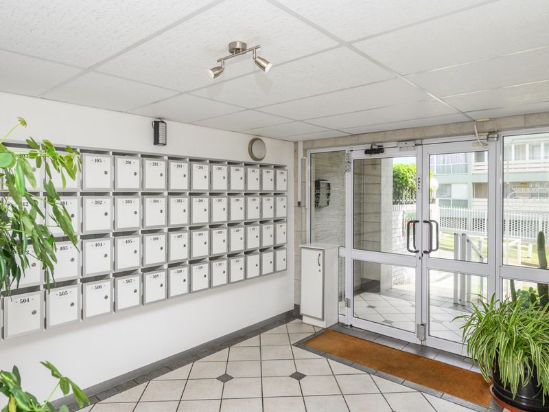 A clean and functional apartment building entrance lobby featuring a wall of individual mailboxes, tiled flooring, and secure glass entry doors.