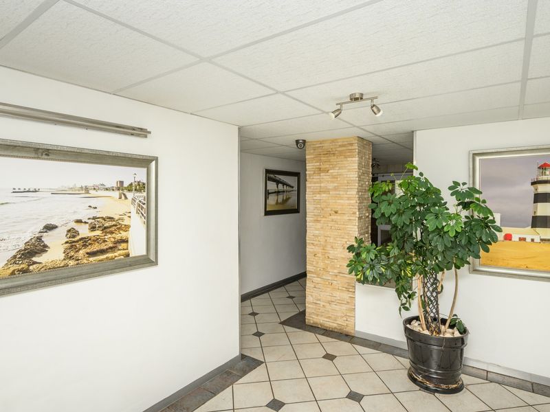 A well-lit apartment hallway featuring a stone veneer accent pillar, ceramic tiled flooring, and a drop ceiling with integrated lighting.