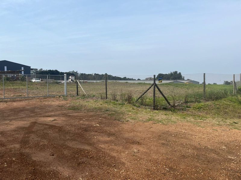 A view of a vacant agricultural plot featuring a metal gate, chain-link perimeter fencing, and an unpaved access area.