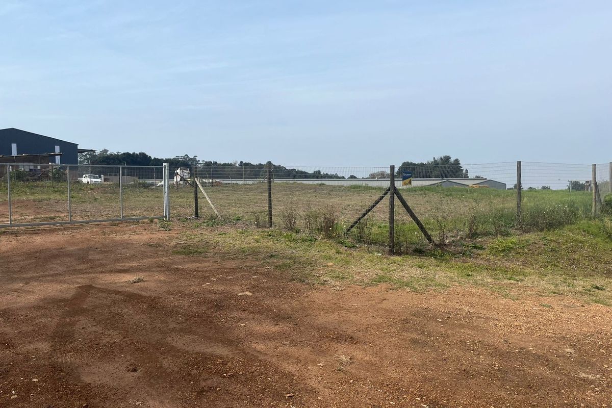 A view of a vacant agricultural plot featuring a metal gate, chain-link perimeter fencing, and an unpaved access area.