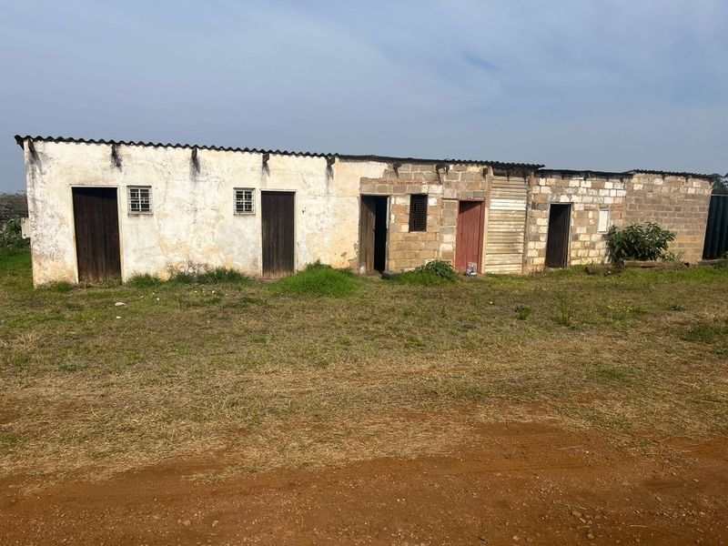 A single-story agricultural outbuilding featuring multiple entry points, cinder block construction, and a corrugated metal roof set on a rural plot.