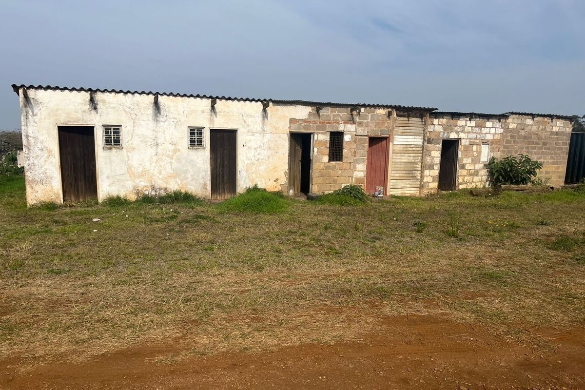 A single-story agricultural outbuilding featuring multiple entry points, cinder block construction, and a corrugated metal roof set on a rural plot.