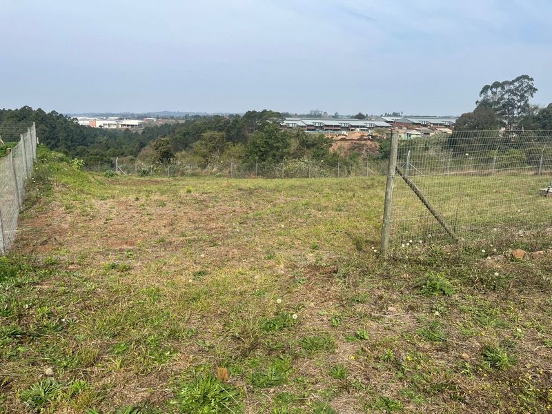A view across the vacant agricultural land, featuring perimeter wire mesh fencing and distant views of the surrounding landscape and nearby developments.