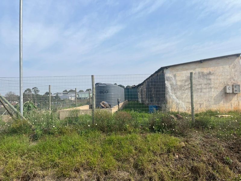 View of the rear property area featuring wire mesh fencing, a water storage tank, and a utility structure with weathered exterior walls.