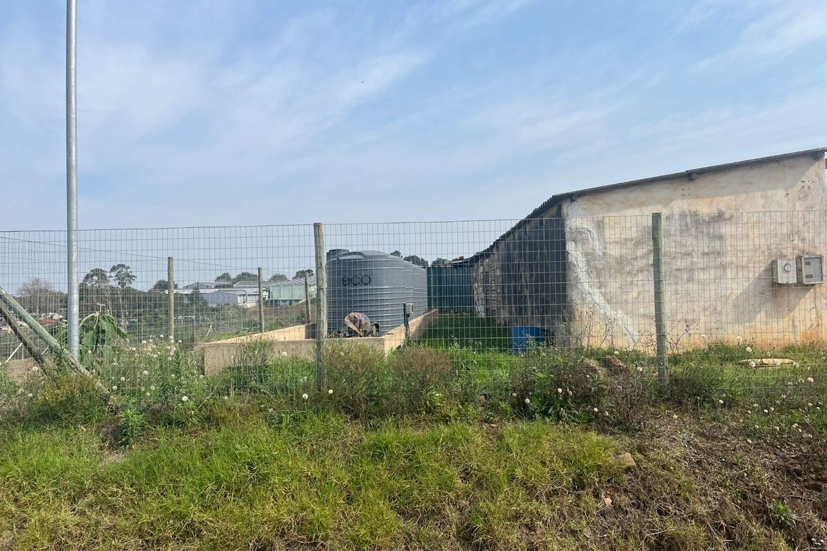 View of the rear property area featuring wire mesh fencing, a water storage tank, and a utility structure with weathered exterior walls.