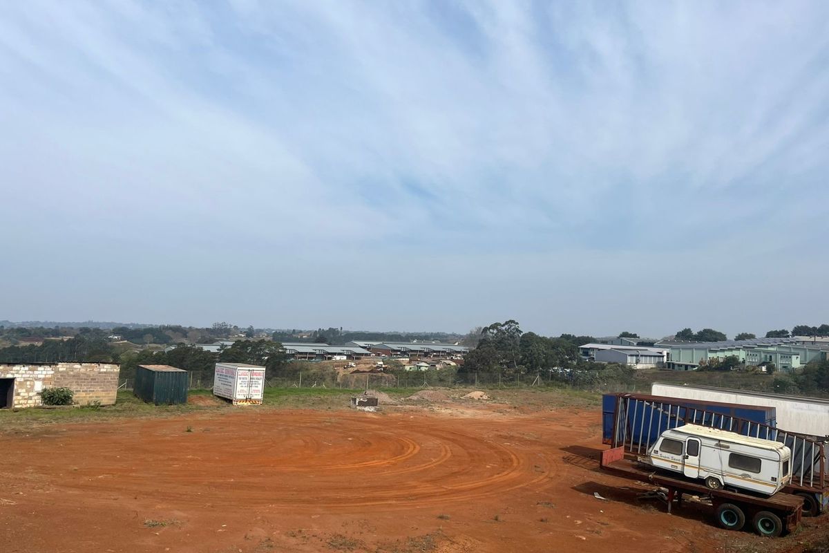 An elevated view of a vacant agricultural plot featuring unpaved ground and perimeter fencing with surrounding industrial buildings in the distance.