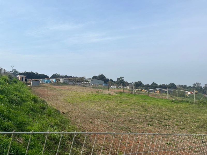 A view of an open agricultural land plot featuring sloped terrain and perimeter wire mesh fencing.