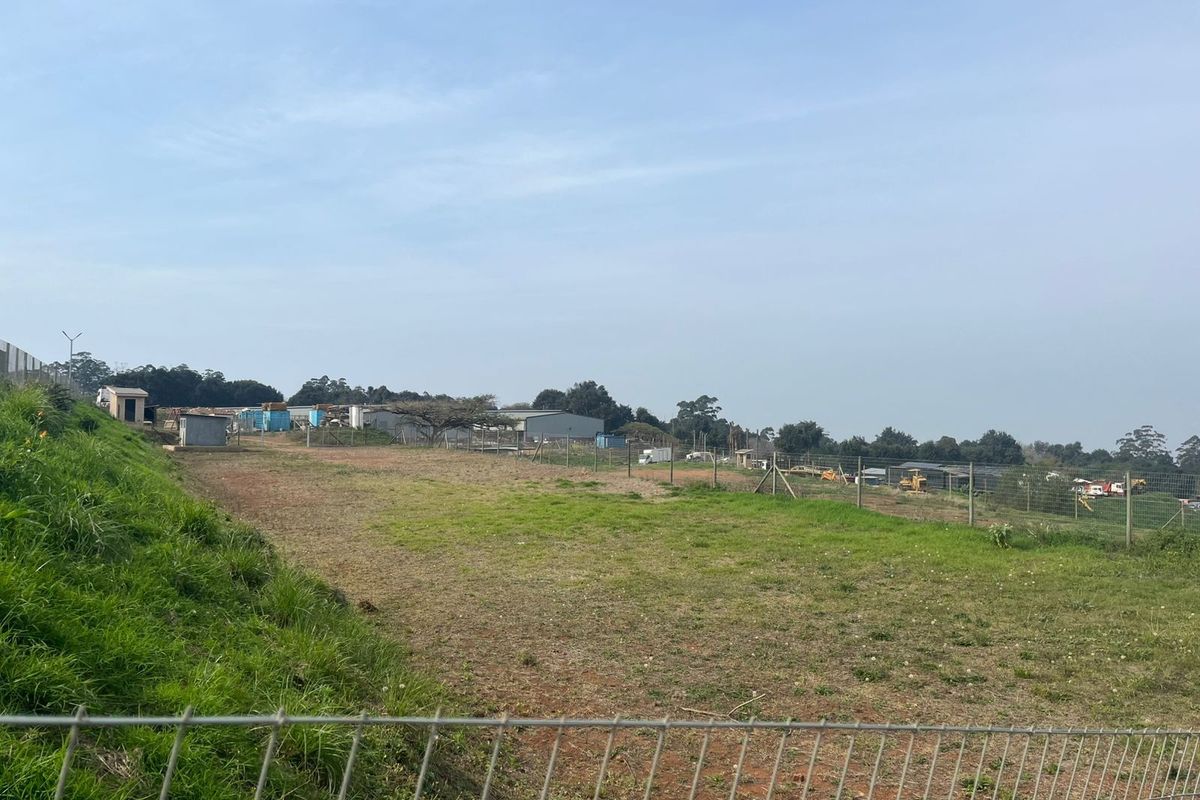A view of an open agricultural land plot featuring sloped terrain and perimeter wire mesh fencing.