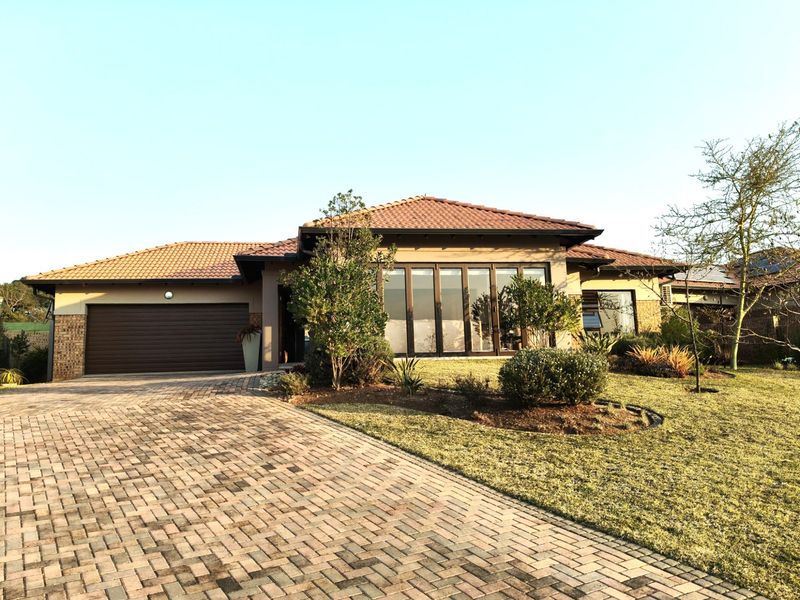 A well-maintained retirement village home featuring a brick-paved driveway, double garage, and modern aluminium stacker doors opening to a landscaped front garden.