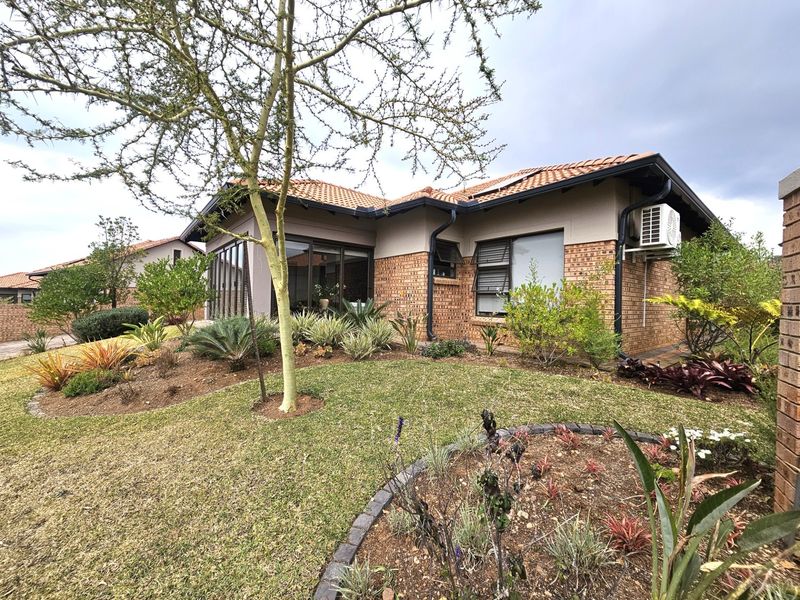 A well-maintained retirement village home featuring a face-brick exterior, tiled roof, landscaped garden, and integrated air conditioning unit.