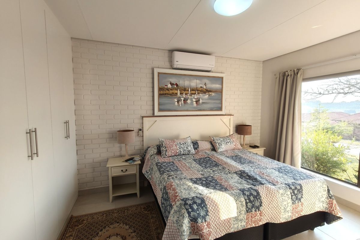 A well-maintained bedroom featuring a brick accent wall, built-in wardrobes, split-system air conditioning, and large windows providing natural light.