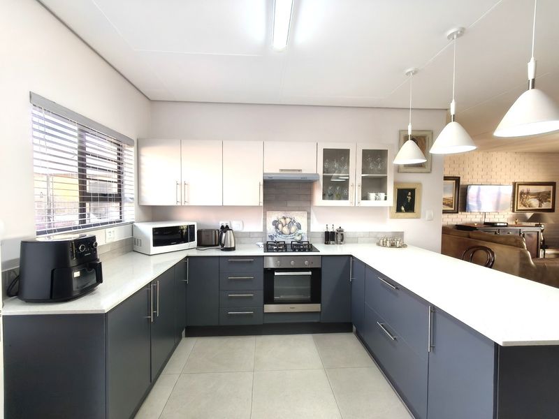 Modern U-shaped kitchen featuring dark lower cabinetry, white upper cabinets, stone countertops, integrated gas hob, and oven, complemented by stylish pendant lighting.