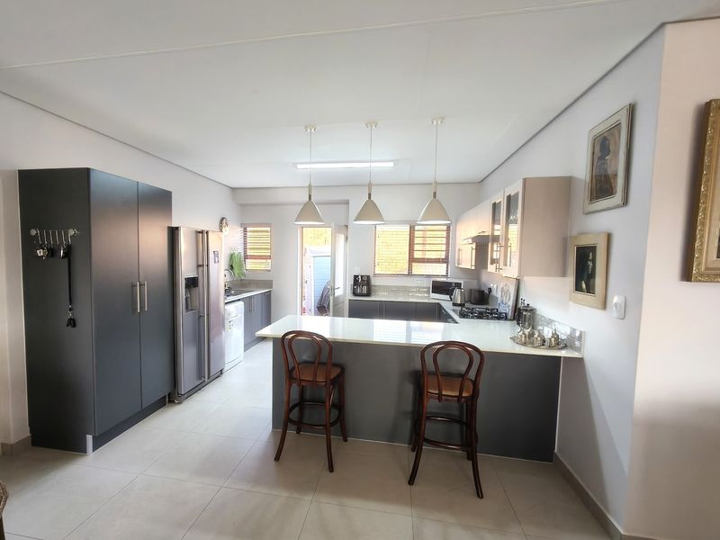Modern kitchen featuring a central island with stone countertops, ample built-in cabinetry, gas hob, and sleek pendant lighting in an open-plan layout.