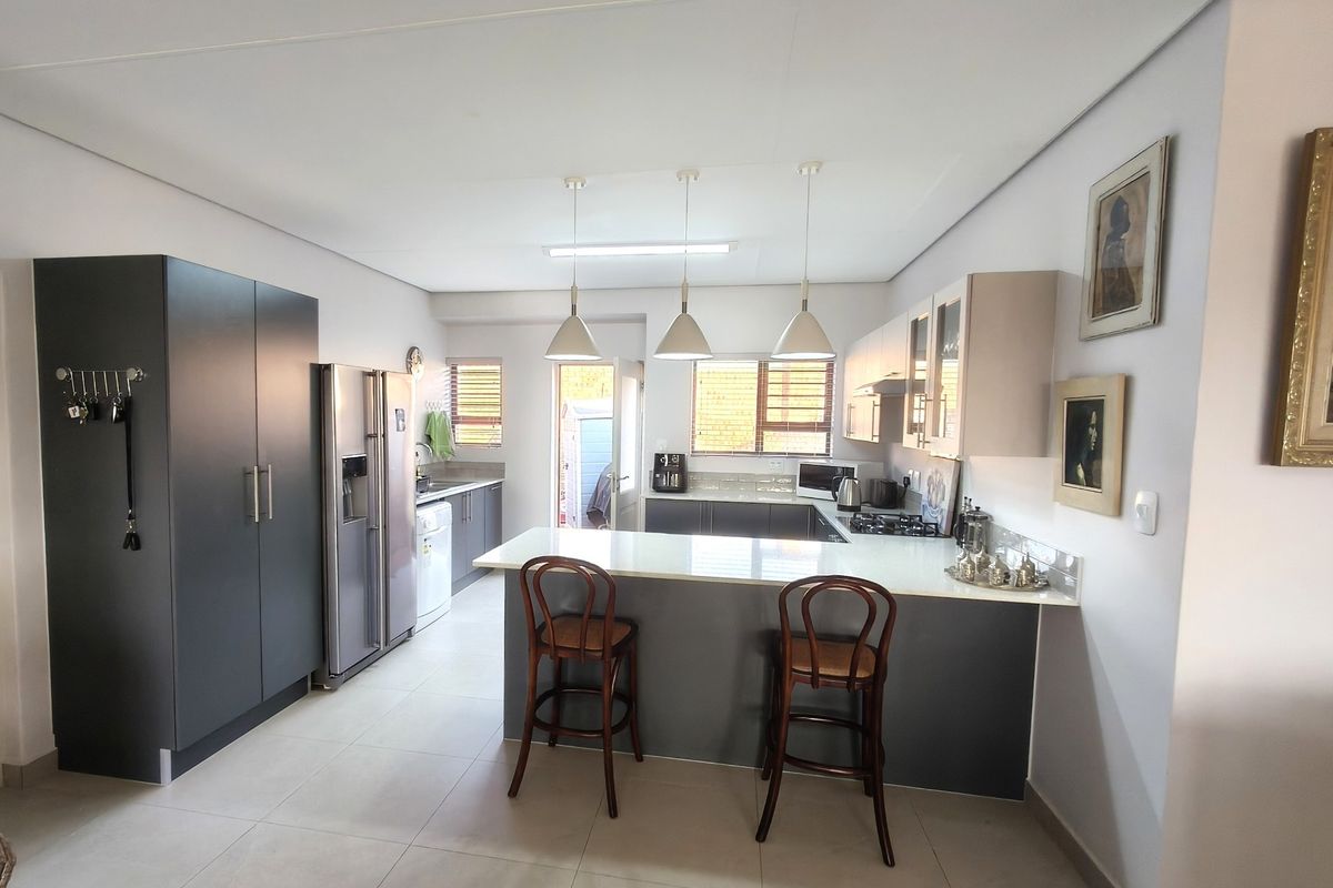 Modern kitchen featuring a central island with stone countertops, ample built-in cabinetry, gas hob, and sleek pendant lighting in an open-plan layout.