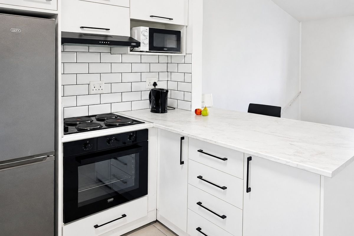Modern kitchen featuring white cabinetry, marble-look countertops, subway tile backsplash, and built-in appliances including an oven, hob, and extractor fan.