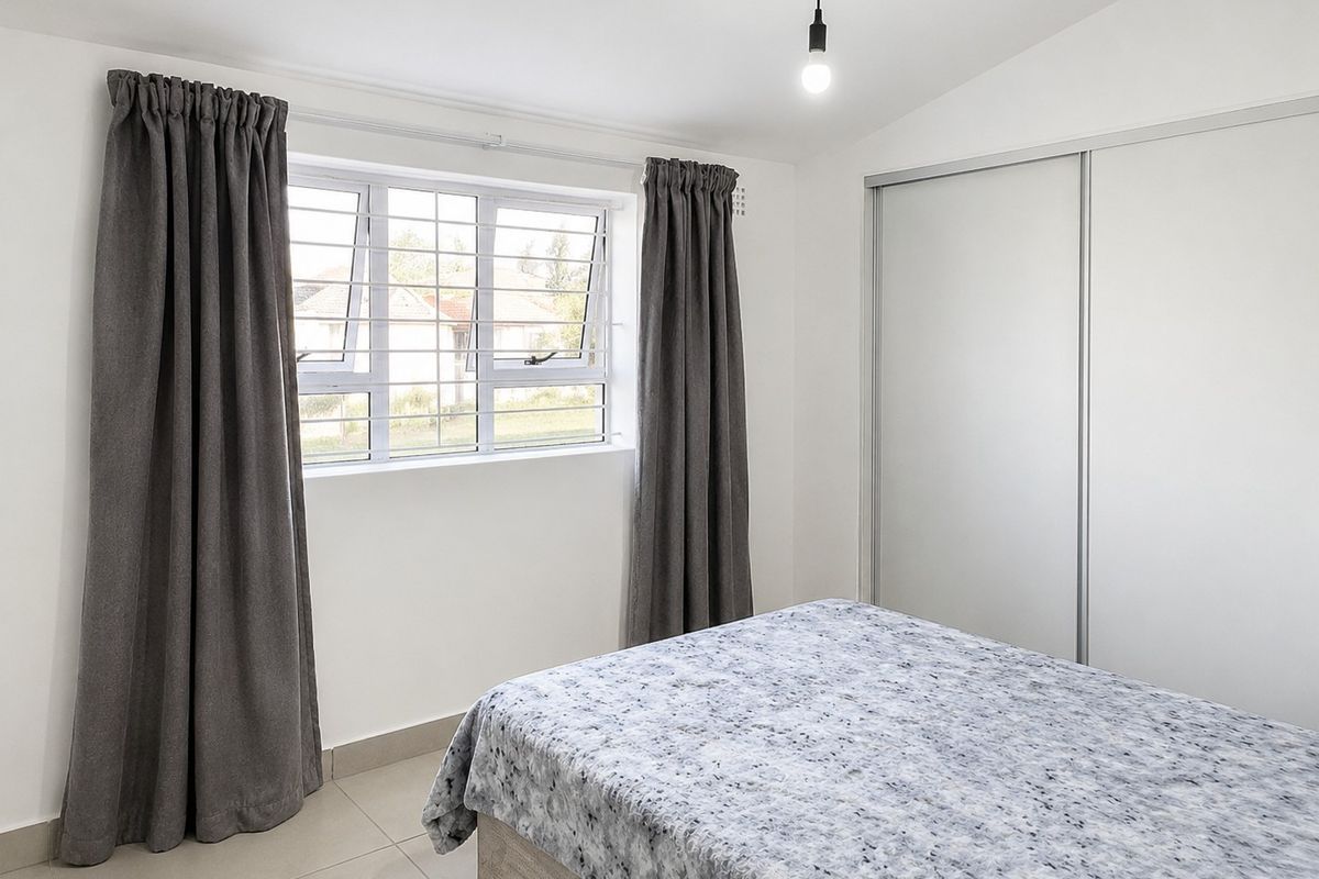 A bright bedroom featuring neutral tiled flooring, a built-in sliding door wardrobe, and a window fitted with security bars.