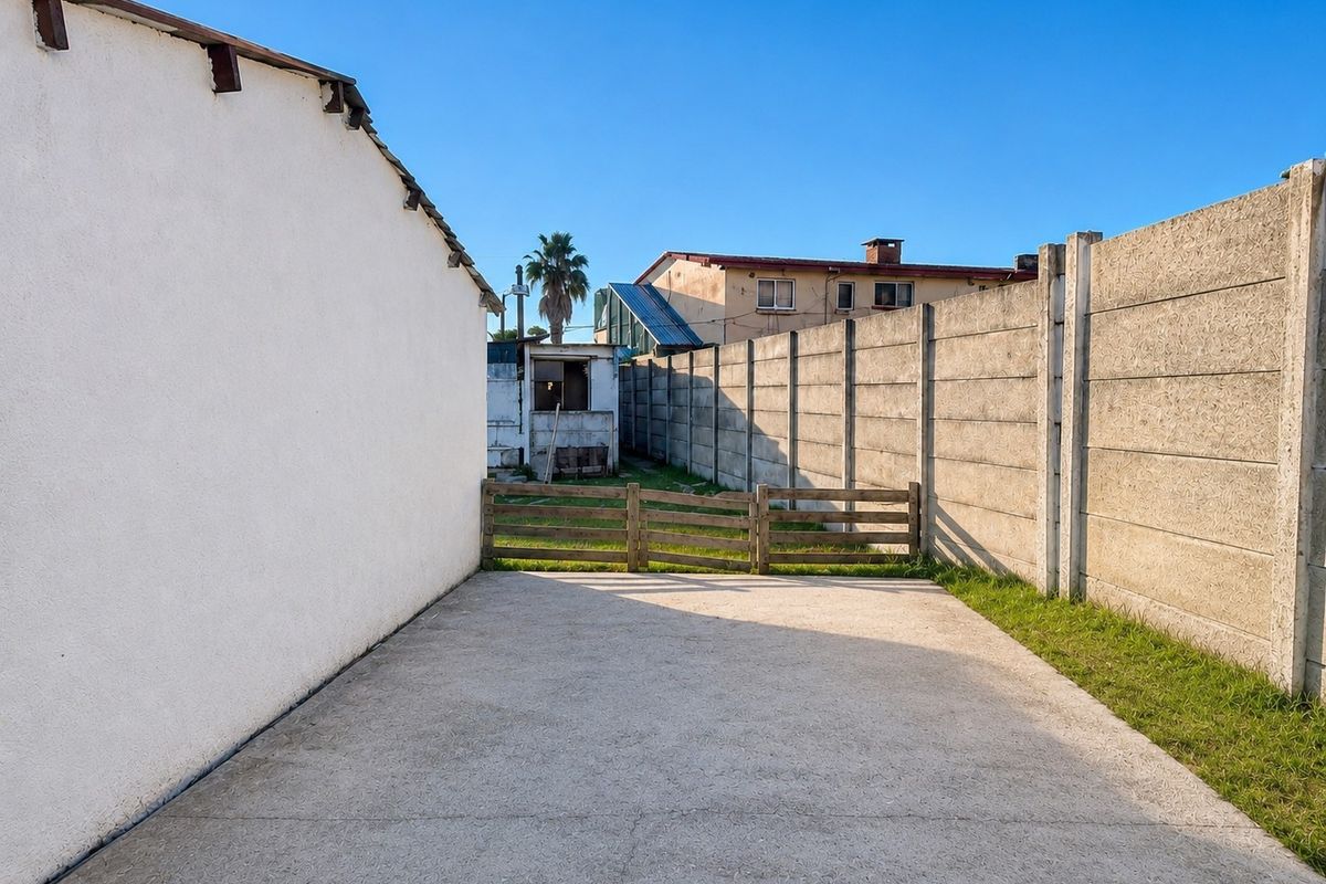Rear exterior area featuring a concrete paved surface, enclosed by a precast concrete boundary wall and a small timber fence.