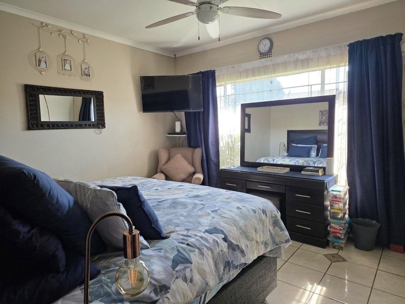 A bedroom featuring tiled flooring, a ceiling fan, and a large window allowing natural light into the space.