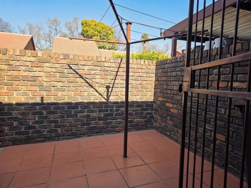 A private rear courtyard featuring tiled flooring, enclosed by brick boundary walls and secured with a metal gate.