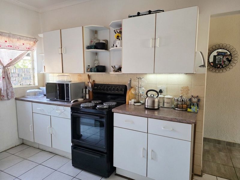 A functional kitchen featuring white cabinetry, laminate countertops, a tiled backsplash, and a freestanding stove, with ceramic floor tiles throughout.