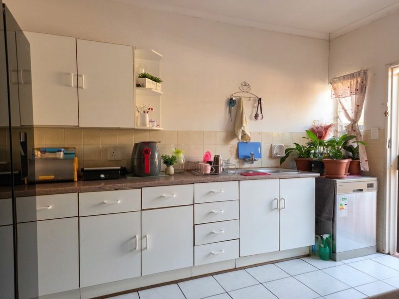 A functional kitchen featuring white cabinetry, laminate countertops, tiled backsplash, and tiled flooring, offering a practical layout for daily meal preparation.