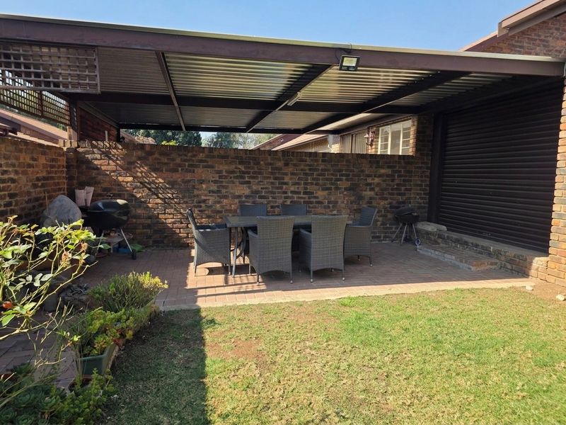 A covered outdoor patio area featuring paved flooring, a brick boundary wall, and a metal roof structure, ideal for outdoor dining and entertaining.