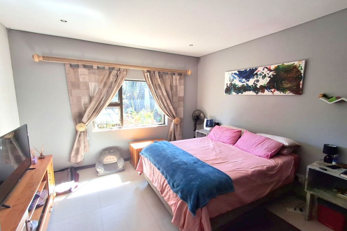 A well-lit bedroom featuring neutral grey walls, tiled flooring, and a large window with natural light.