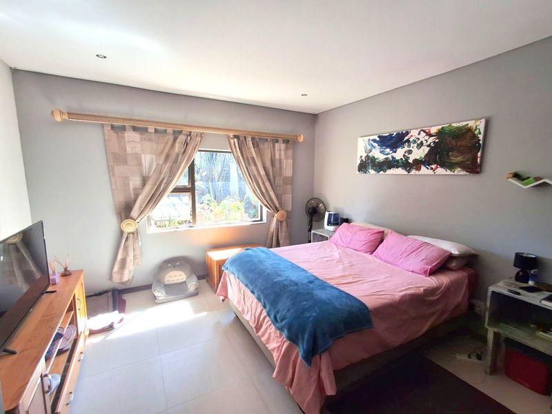 A well-lit bedroom featuring neutral grey walls, tiled flooring, and a large window with natural light.
