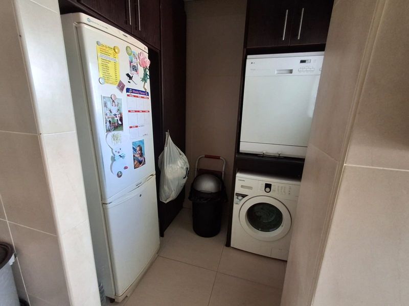 A functional laundry area featuring built-in cabinetry, tiled flooring, and space for a washing machine and dishwasher.