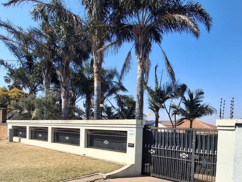 Front exterior view of the property featuring a secure perimeter wall with integrated metal fencing, electric security wires, and mature palm trees.