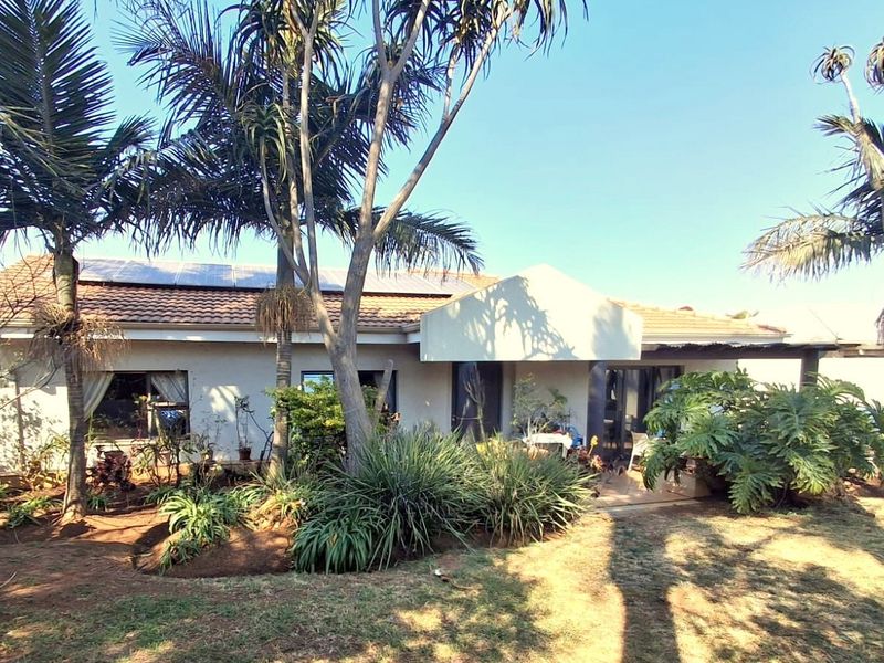 Rear view of the house featuring a tiled roof with solar panels, a covered patio area, and a mature landscaped garden.