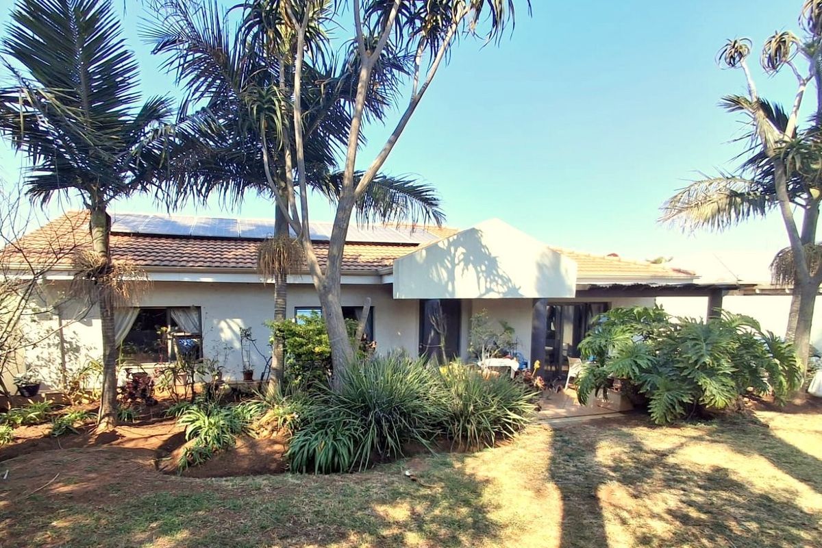 Rear view of the house featuring a tiled roof with solar panels, a covered patio area, and a mature landscaped garden.