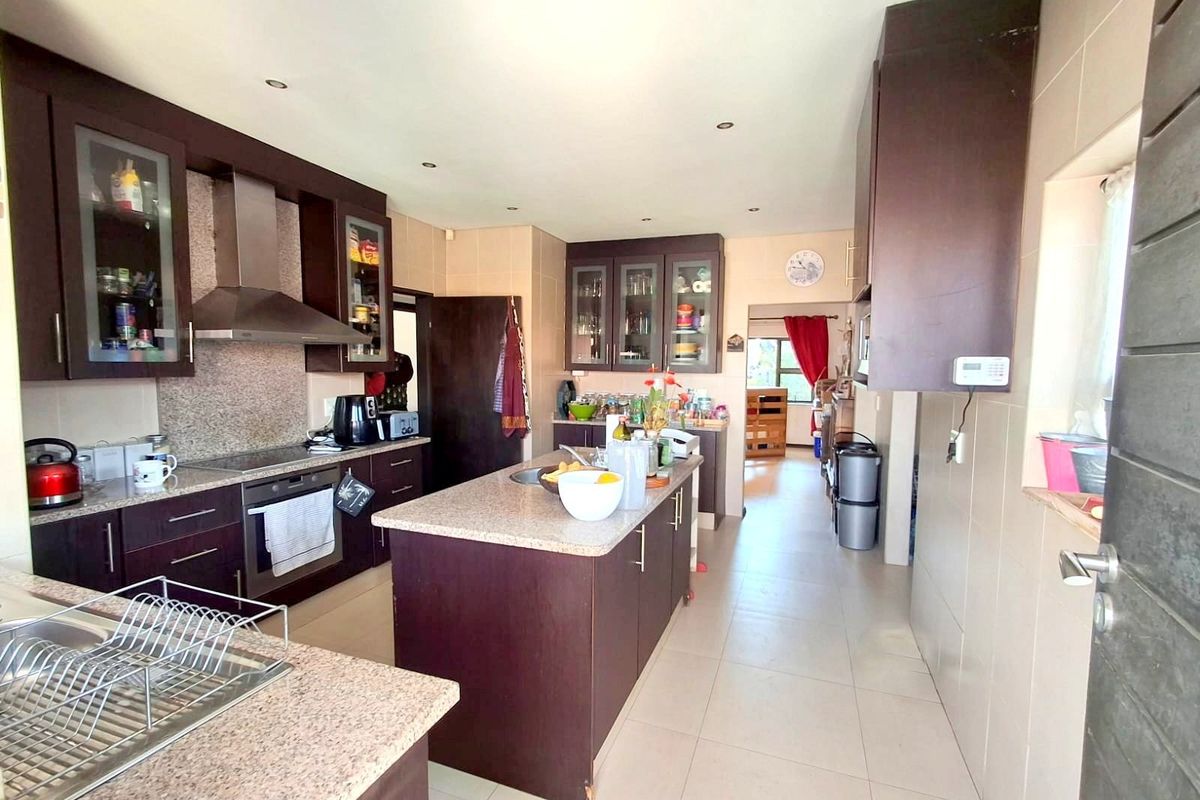 Spacious kitchen featuring dark wood cabinetry, granite countertops, a central island, and built-in appliances with tiled flooring throughout.