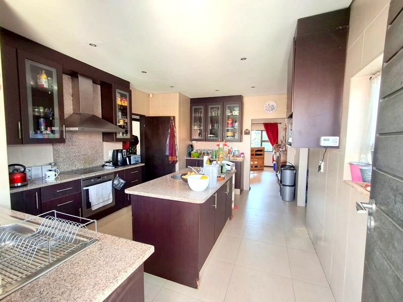 Spacious kitchen featuring dark wood cabinetry, granite countertops, a central island, and built-in appliances with tiled flooring throughout.