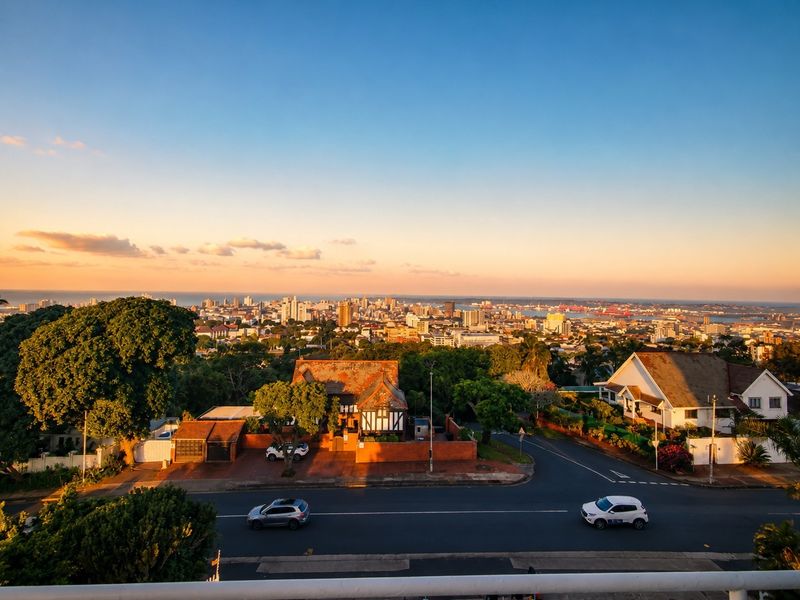 A scenic elevated view overlooking the surrounding neighborhood, suburban streets, and the distant city skyline at sunset.