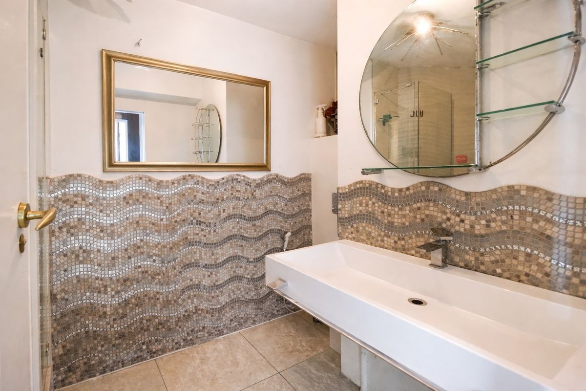 Bathroom featuring a wall-mounted basin, mosaic tile backsplash, and a shower enclosure with glass shelving.