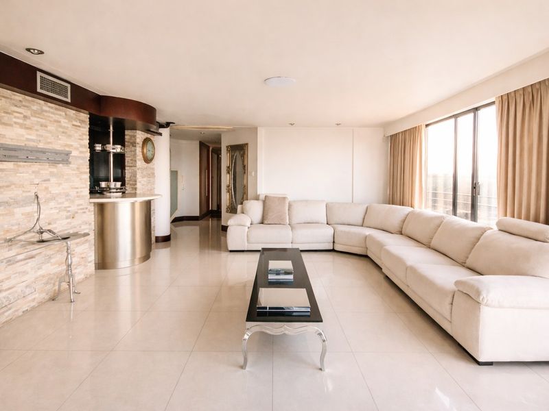 Spacious living room featuring a stone accent wall, integrated bar area, polished tile flooring, and large windows providing ample natural light.