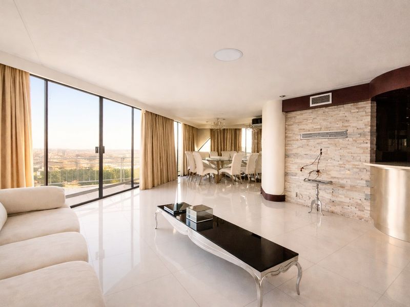 Spacious open-plan living and dining area featuring polished tile floors, a striking stone feature wall, and expansive floor-to-ceiling glass doors with panoramic views.