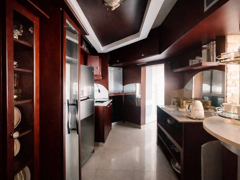 A kitchen featuring dark wood cabinetry, stone countertops, and tiled flooring, with integrated storage and recessed ceiling lighting.