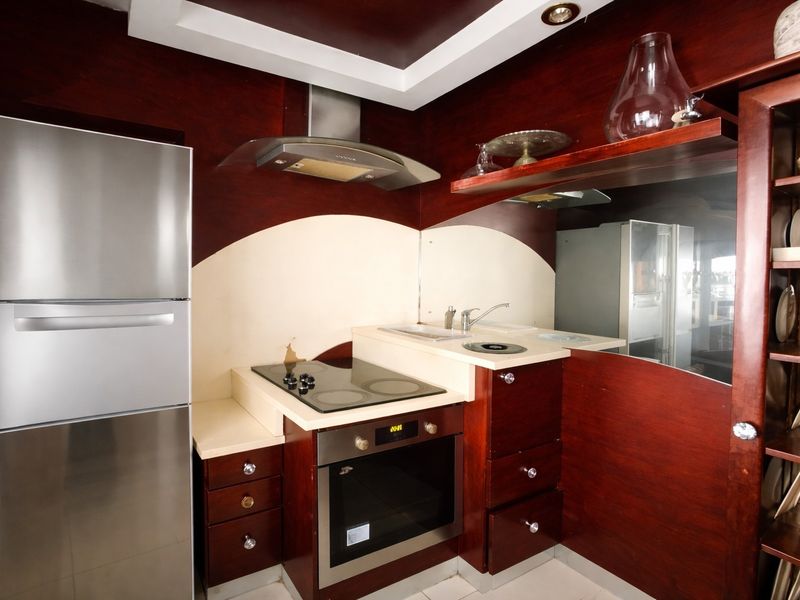 Compact kitchen featuring dark wood cabinetry, built-in oven, electric cooktop, stainless steel extractor fan, and a mirrored splashback.